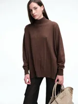 Sweater de tejido de punto color marrón, con cuello alto, corte amplio y tajos laterales en el ruedo. Presenta una costura vertical central en el frente y mangas largas con puños acanalados.