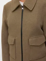 Campera estilo biker corta de punto interlock, con cuello camisero, cierre frontal metálico y bolsillos delanteros con solapa y broches a presión. Presenta un diseño estructurado y liviano sin forrería.