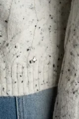Sweater de punto con textura de ochos, color gris melange con motas oscuras, cuello redondo y mangas largas con terminación acampanada.