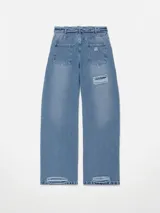Pantalón de jean estilo wide leg con diseño de cintura cruzada y tiro bajo. Presenta un lavado azul medio con efecto desgastado y un detalle de rotura en la rodilla derecha.