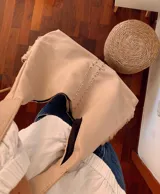 Cartera estilo hobo de cuero sintético color beige, con flecos laterales, detalle de tachas metálicas verticales en el frente y aplique con estrellas grabadas en la base.