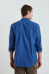 Camisa azul de manga larga con cuello clásico, cierre con botones y bolsillo en el pecho.