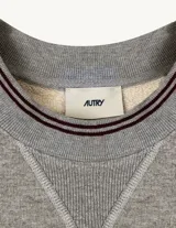 Buzo de cuello redondo color gris melange, con estampa frontal de la marca Autry en tipografía universitaria. Presenta detalles de ribete a rayas en el cuello y los puños, con costuras reforzadas en el escote.