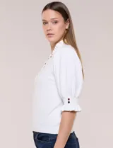 Buzo de algodón blanco con cuello mao y volados, manga tres cuartos abullonada y botones metálicos decorativos en la parte frontal.