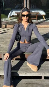 Conjunto de dos piezas de tejido de punto color gris oscuro, compuesto por un buzo tipo hoodie corto con cierre frontal y un pantalón de tiro bajo con corte acampanado.
