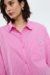 Camisa oversize de popelina a rayas celestes y blancas, con cuello camisero, manga larga con puños abotonados, cierre frontal con botones y un bolsillo en el pecho con etiqueta bordada.