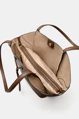 Bolso de hombro tipo maxi shopper color marrón, con doble asa y estructura flexible que se pliega hacia afuera. Presenta un detalle de tira ajustable con cordón en el centro frontal. Incluye un compartimento interior extraíble con cierre de cremallera y cierre principal mediante botón imantado.