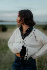 Saco tipo cardigan de punto color blanco con detalles de pespuntes decorativos en color negro a lo largo de los bordes y costuras. Presenta cuello en V, cierre frontal con botones y mangas largas.