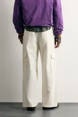 Pantalón cargo relaxed fit de color blanco, confeccionado en tejido de algodón. Presenta bolsillos de plastrón con solapa en las perneras y cierre frontal con cremallera y botón.