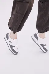 Zapatillas de diseño urbano en color blanco con inserciones en gris oscuro, cordones al tono y detalle de estrella bordada en el lateral.