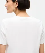 Remera de algodón de corte clásico con cuello redondo y manga corta. Presenta un diseño estampado con pequeños lazos formados por aplicaciones de hotfix brillantes distribuidos por toda la prenda.