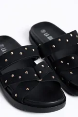 Sandalias negras de doble tira con tachas doradas, suela plana y diseño cómodo.
