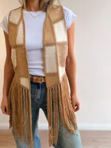 Chaleco de estilo boho con diseño patchwork en tonos beige y tostado, confeccionado con efecto gamuza y pespuntes decorativos. Presenta diseño abierto sin cierre y flecos largos en el ruedo.