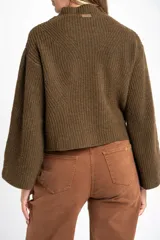 Polera de lana oversize color beige melange, con cuello alto, mangas largas acampanadas y diseño de tejido acanalado con tramas direccionales.