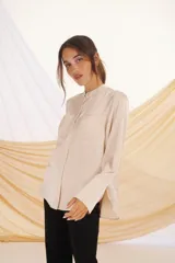 Camisa color beige de corte clásico, con cuello mao, cierre frontal con botones ocultos, mangas largas con puños abotonados y dos bolsillos de parche en el pecho.