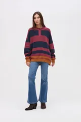 Buzo de punto con diseño de rayas horizontales en tonos bordó, azul marino y mostaza. Presenta cuello tipo polo con cartera de botones, mangas largas y calce holgado.