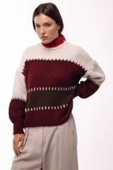 Sweater de tejido de punto grueso con diseño de bloques de color en tonos beige, marrón y bordó. Presenta un corte relajado, mangas amplias y detalles de costuras visibles en contraste que separan las franjas de color.