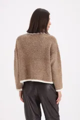 Saco tipo cardigan de tejido bouclé en color visón, con bordes y detalles en color crema. Presenta cuello redondo, cierre frontal con botones y dos bolsillos delanteros con solapa.