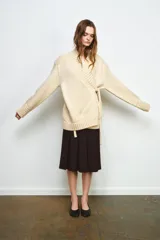 Chaqueta cruzada de punto color beige con manga larga, cuello smoking y cierre frontal con lazada. Presenta detalles de calados en los puños.