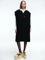 Chaleco largo de corte recto y textura de peluche, con cuello en V y cierre frontal de botones. Diseño sin mangas con silueta holgada.