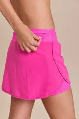 Pollera deportiva color rosa fucsia, con estampado en relieve de texto. Es de corte corto con ruedo redondeado y cuenta con shorts internos.