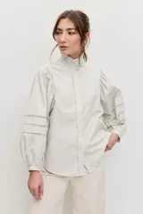 Camisa de manga larga color marrón, con cuello alto con volados, botonadura frontal y detalles calados en las mangas abullonadas.