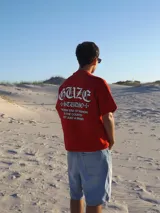 Remera roja de algodón con estampado en el dorso con el texto "GUZE + STUDIO + THE NEW ERA OF FASHION IN THE COUNTRY NOT JUST A BRAND" en color blanco.