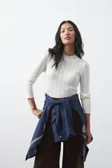 Polera de tejido de punto con textura calada y diseño de líneas verticales acanaladas. Presenta cuello alto y mangas largas con puños delicados, de silueta entallada.