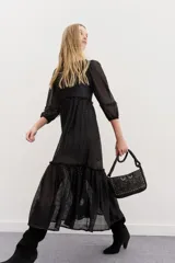 Vestido largo de tul negro con bordados de lentejuelas y canutillos, mangas tres cuartos abullonadas, cintura fruncida y falda con volado en el ruedo.