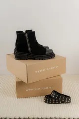 Bota corta de gamuza marrón con puntera de cuero liso, suela track negra y correa desmontable con tachas metálicas.