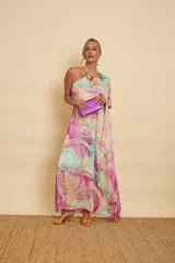 Vestido largo con diseño marmolado en tonos celestes, rosados y amarillos, de corte asimétrico con un solo hombro y manga larga acampanada.