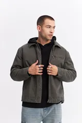 Campera de canvas color gris oscuro con cuello camisero, cierre frontal y bolsillo con cierre en el pecho. Presenta un diseño de estructura firme con estilo utilitario.