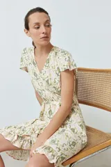 Vestido corto cruzado con estampado abstracto en tonos verde oliva, amarillo y rosa. Tiene escote en V, mangas cortas con volados y falda con volados en el ruedo. Se ata a la cintura con un lazo.