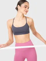 Top deportivo gris de soporte bajo, ideal para pilates y yoga. Tiene escote redondo, tirantes finos ajustables que se cruzan en la espalda y almohadillas removibles.