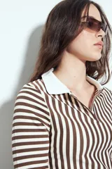 Remera de manga larga a rayas verticales verdes y blancas, con cuello polo y cierre frontal de botones. Presenta un diseño ajustado al cuerpo.