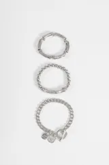 Set de tres pulseras plateadas de diseño variado: una con cuentas cilíndricas, una con cuentas esféricas y una pulsera de cadena con dijes colgantes y cierre de barra.