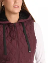 Chaleco capitoneado de color negro con diseño acolchado en forma de rombos. Presenta capucha integrada con cordones de ajuste, cierre frontal completo y bolsillos laterales con cierre a presión.