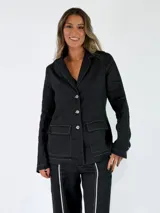 Blazer negro de lino con costuras a contratono en color blanco, bolsillos frontales con solapa y cierre de botones.