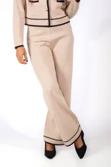 Conjunto de dos piezas compuesto por saco tipo cardigan y pantalón a juego. El saco es de punto en color beige, con cuello redondo, cierre frontal de botones dorados y ribetes en contraste color negro en el borde, puños y bolsillos frontales. El pantalón es de corte recto y tiro alto, confeccionado en el mismo tejido de punto.