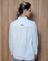 Camisa blanca de algodón con cuello alto tipo mao y volados sutiles a lo largo de la botonadura frontal. Presenta mangas largas con frunces en los hombros y botones frontales.