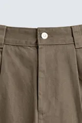 Pantalón de corte baggy fit confeccionado en tejido de algodón con estructura diagonal y efecto lavado. Presenta cintura con pliegues frontales, bolsillos laterales, bolsillos traseros de vivo y un bolsillo lateral adicional con doble vivo en la pernera. Cierre frontal con cremallera y botón.