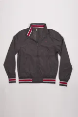 Campera liviana de nylon color gris oscuro, con cierre frontal completo, cuello subido y puños y cintura acanalados con rayas en rojo y blanco. Presenta logo bordado en el pecho y bolsillos laterales con cierre.