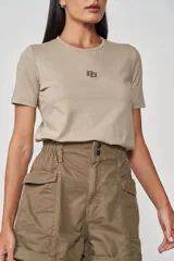 Remera color beige de corte clásico con cuello redondo y logo metálico en el pecho.