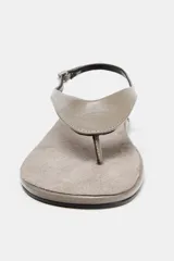 Sandalia plana tipo ojota confeccionada en piel, con diseño de punta redonda, tira entre los dedos y tira trasera ajustable con hebilla metálica.