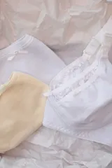 Kit maternal compuesto por un soutien blanco de algodón con puntilla y dos bombachas de algodón, una blanca y otra color piel, con moños decorativos.