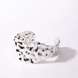 Brazalete rígido plateado con textura irregular y aberturas.