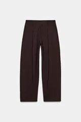 Pantalón marrón de tiro medio y corte carrot wide leg. Presenta trabillas en la cintura, bolsillos laterales ocultos en la costura, pespuntes marcados a tono y una hebilla decorativa en la espalda. Cierre frontal con cremallera, botón y ganchos metálicos.