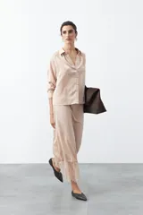 Camisa de satén color beige, con cuello clásico, mangas largas y cierre frontal con botones forrados. Presenta un corte recto y fluido.