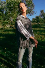 Chaleco tejido de lana merino color gris con diseño de trenzas, estilo oversized y más largo en la parte trasera.