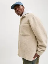 Sobrecamisa de textura teddy, color beige, con cuello camisero, cierre frontal de botones, mangas largas con puños abotonados y dos bolsillos frontales en el pecho.
